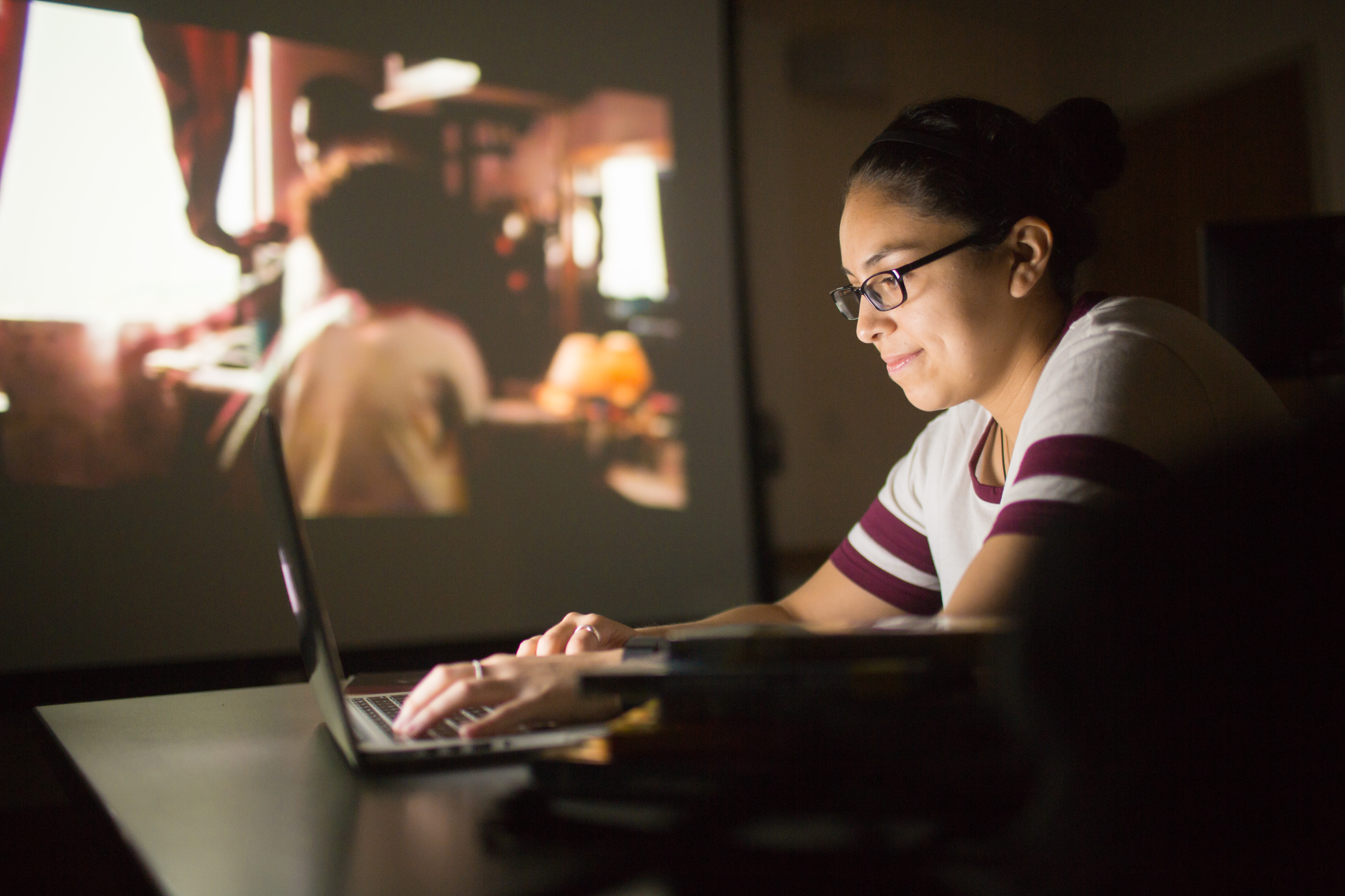student working on computer with film showing in background