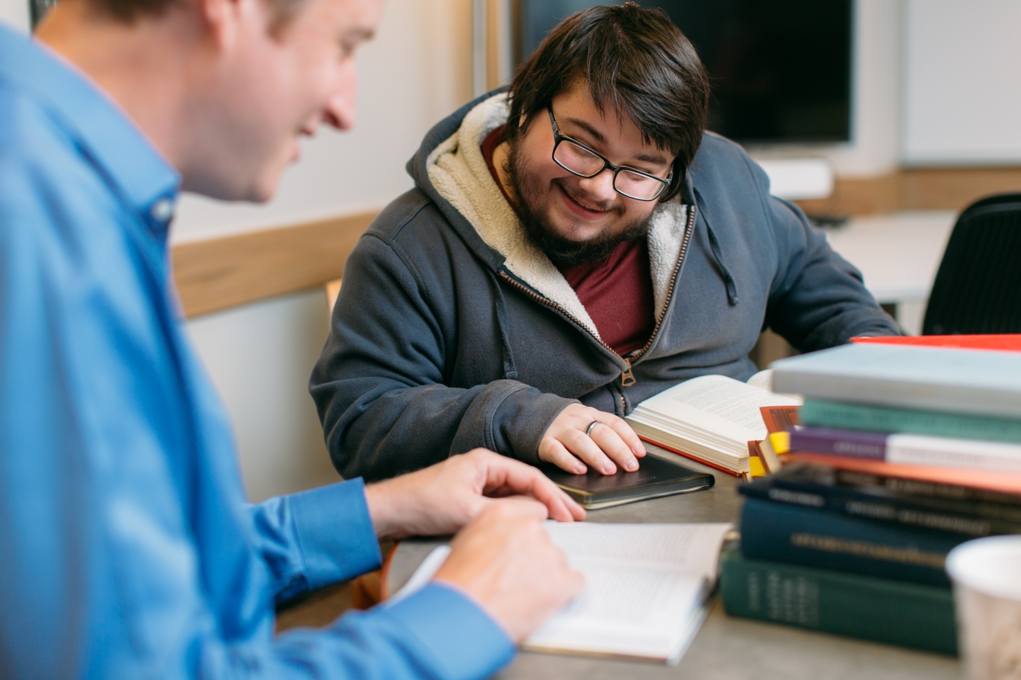 Two students engaged in conversation with a stack of books on their table