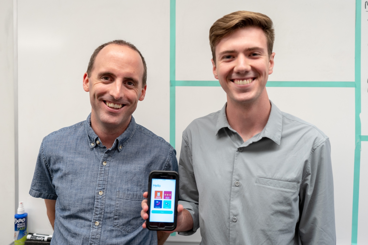 two men smiling and showing an iPhone screen