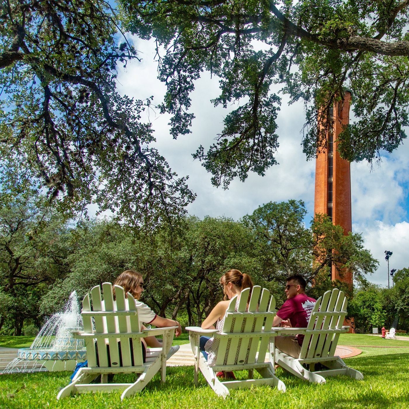 three students sit by miller fountain in adirondack chairs