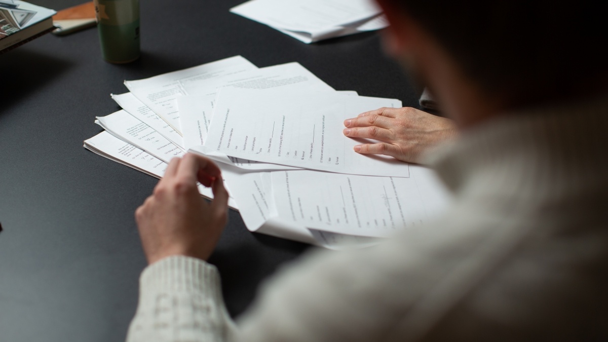 Over the should look at a person with a pile of papers on a table