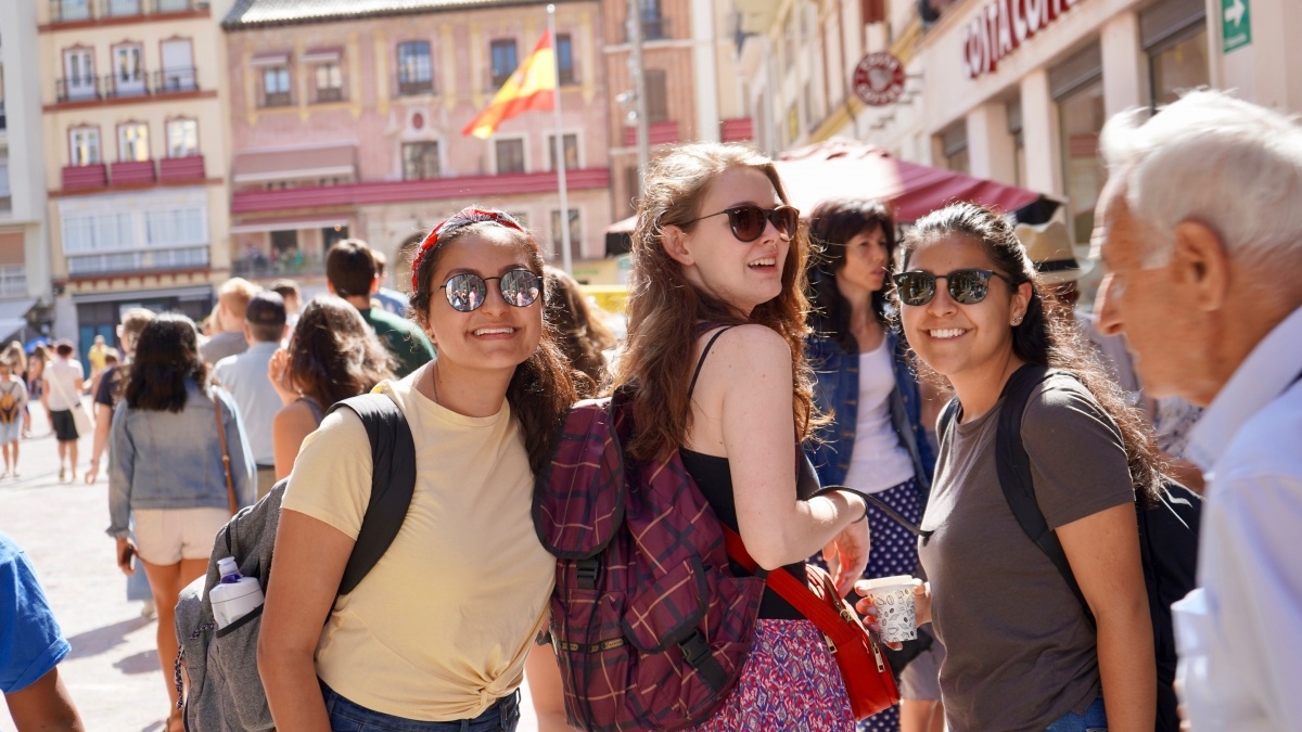 Three women turn to smile while walking along a busy street