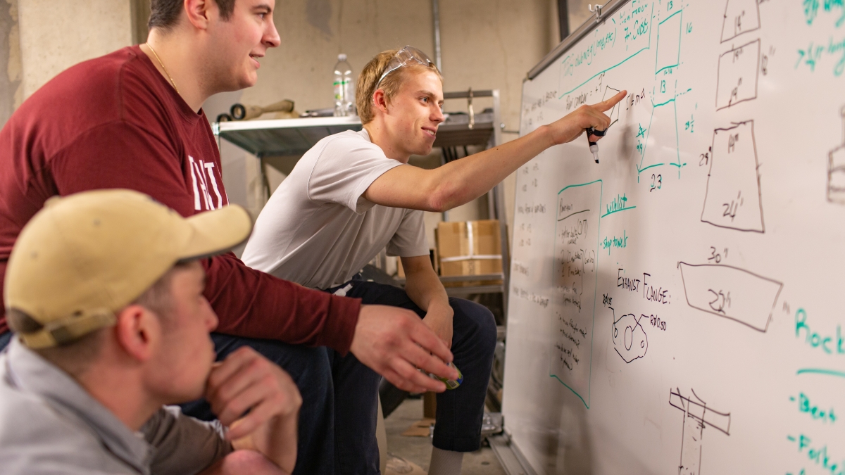 Students writing on a whiteboard discussing a project