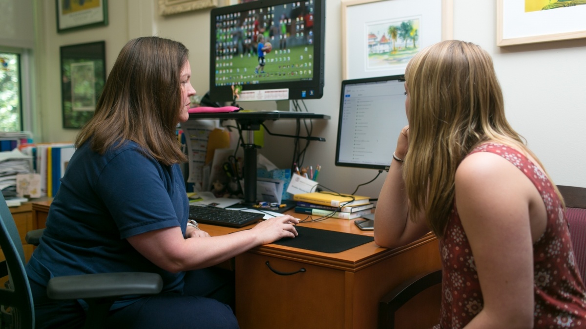 Professor talking to student in her office while typing on computer