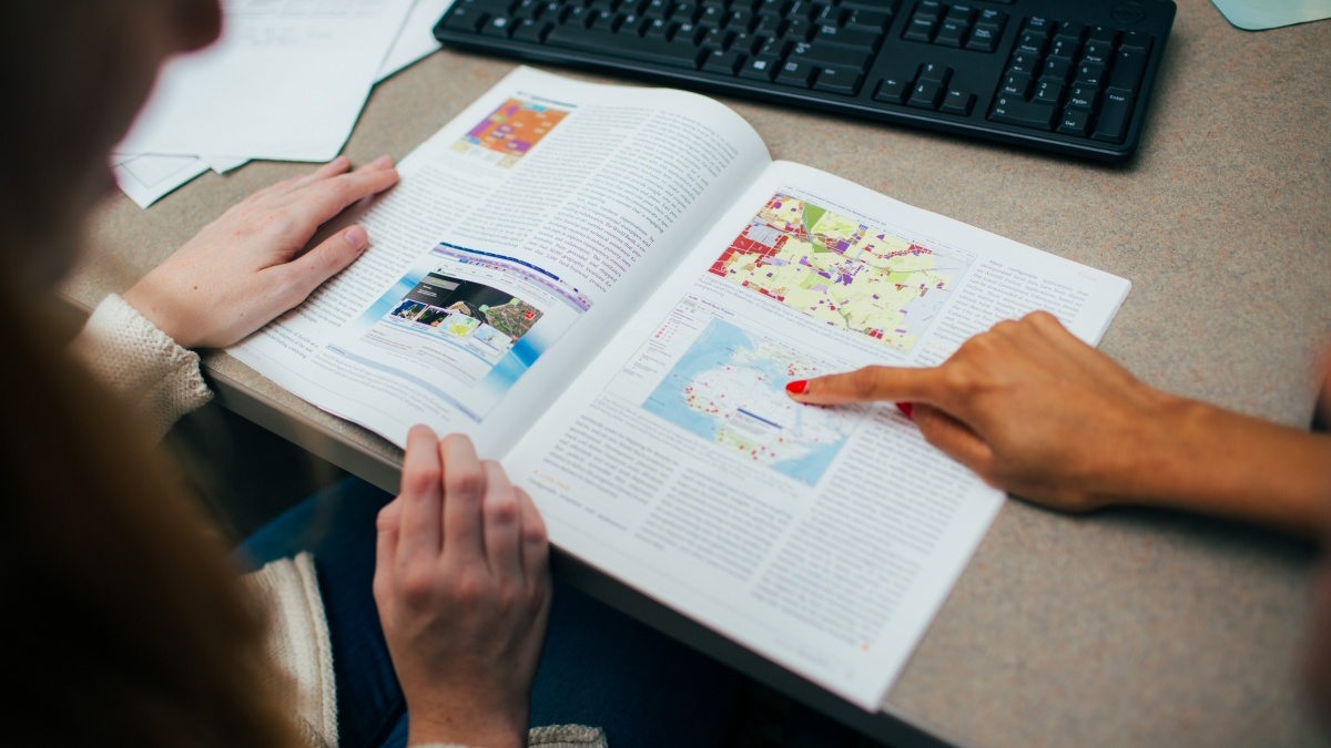 One student pointing to a diagram in a book while another student looks on
