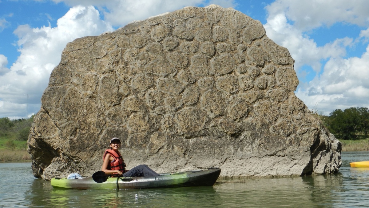 person on a kayak in the river with a big rock as the back landscape