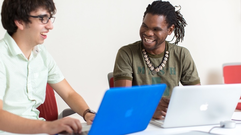 Two students sitting with laptops open.