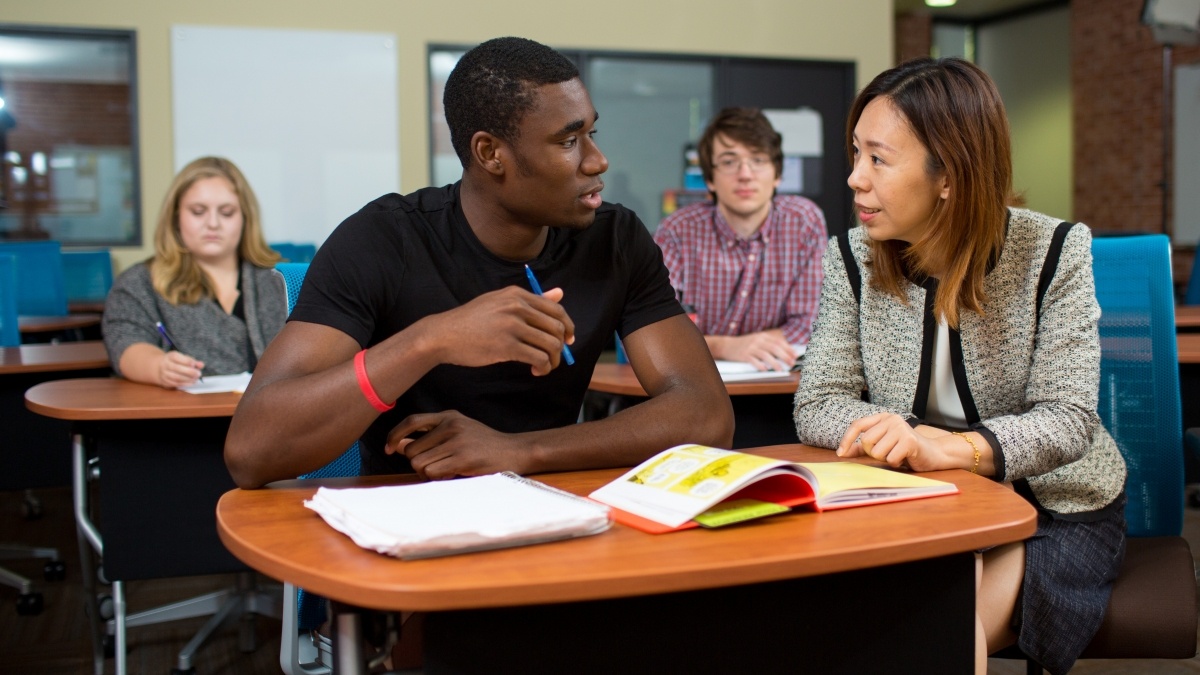 Professor and student in classroom discussion with  other students in the background 